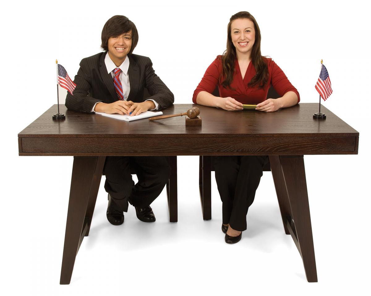 Teen girl and teen boy sitting at a desk for a mock trial.